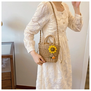 Detail of hand-woven straw bucket bag with sunflower charm and plush pom-poms on long strap