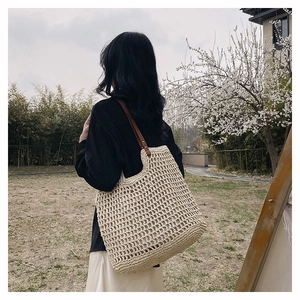 Close-up of woven cream tote bag with brown leather straps and metal rivets detail