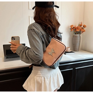 Sac à bandoulière en similicuir rose avec papillon métallique porté par un mannequin