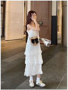 Détail d'un sac en paille avec nœud assorti à une robe longue blanche à plusieurs niveaux