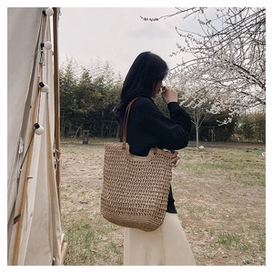 Detail of woven straw tote bag with brown leather shoulder strap in nature setting