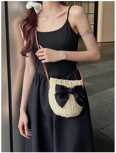 Détail d'un sac bandoulière en paille avec un grand nœud en satin noir et bandoulière