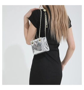 Detail of silver metallic PU leather crossbody bag with gold chain strap on shoulder