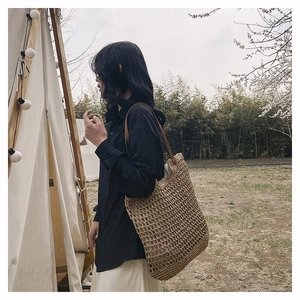 Detail of woven straw tote bag with brown leather straps in an outdoor camping setting
