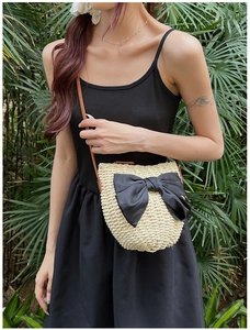 Détail du sac bandoulière en paille beige avec grand nœud en satin noir et sangle réglable