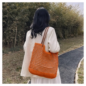 Vibrant orange crochet tote bag with brown leather straps shown in a sunny outdoor setting