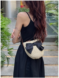 Détail du sac bandoulière en paille avec grand nœud en soie noire porté par un modèle