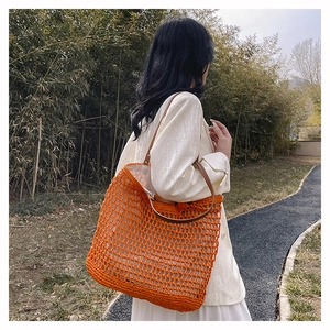 Detail of bright orange knitted tote bag with brown leather strap in an outdoor setting