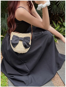 Détail d'un sac bandoulière en paille avec un grand nœud en satin noir et lanière en cuir
