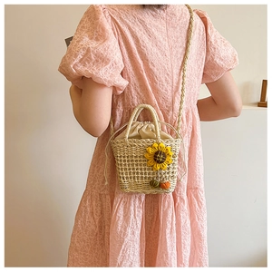 Detailed close-up of straw bucket bag with sunflower accent and pompom on model