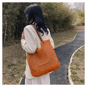 Outdoor lifestyle view of a bright orange woven mesh handbag with brown leather straps