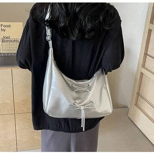Chic metallic silver crescent shoulder bag with a stylish bow detail shown on a model