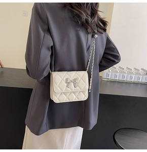 Close-up of beige quilted crossbody bag with silver bow buckle and chain strap on model