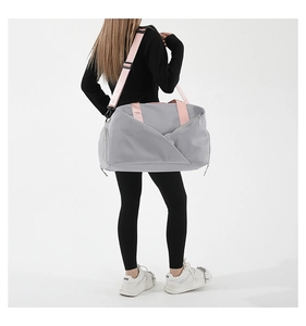 Rear view of a large light grey travel bag with pink straps worn by a model in a studio