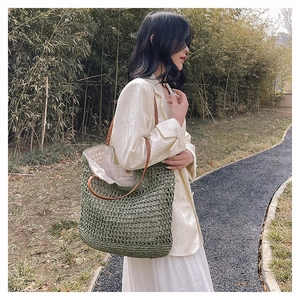 Detail of woven green tote bag with leather straps on model against forest background