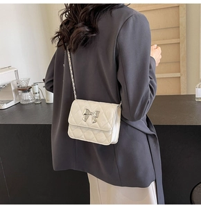 Close-up of a white quilted PU shoulder bag featuring a silver metal bow buckle and chain strap