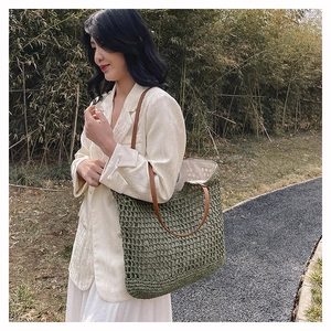 Outdoor shot of a woven grass green tote bag with brown straps in a bamboo garden
