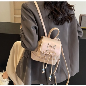 Rear view of a model wearing a small beige PU leather backpack with a bow detail