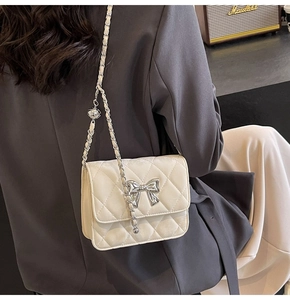 Detail of cream quilted PU crossbody bag with silver bow buckle and chain strap on model