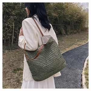 Detail of olive green woven bucket bag with brown leather strap in a natural garden setting