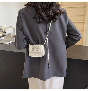 Detail of a white quilted PU mini bag featuring a large silver metal bow on the dark blazer