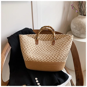Chic two-tone woven straw tote bag with natural bamboo handles on a wooden chair