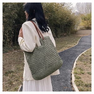 Outdoor model shot of a green woven mesh tote bag with brown leather shoulder straps