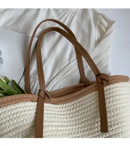 Detail of woven straw tote bag featuring brown leather straps and refined stitching