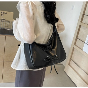 Detail view of black PU leather Hobo bag with bow decoration on a model shoulder