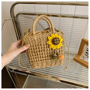 Straw woven handbag with yellow sunflower and colorful pom-poms on a display stand