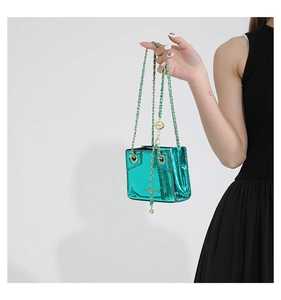 Detail of metallic green mini crossbody bag with gold chain strap held by a model