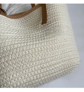 Detailed view of large straw tote bag featuring tight weave texture and brown leather trim