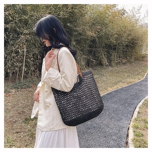 Detail of black woven straw tote bag with brown leather handles on shoulder of a model