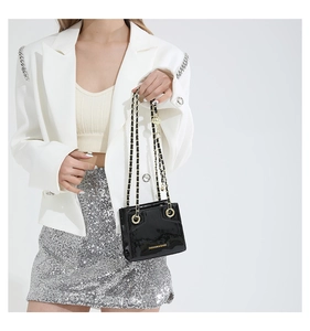 Detail of black glossy faux leather mini handbag with metal chain and fashion text