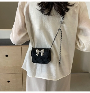 Detail of black quilted mini bag featuring silver bow accent and chain strap worn by model