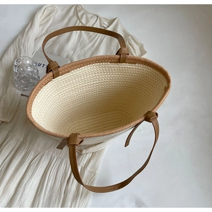 Top view of a woven straw tote bag with brown leather handles on white fabric