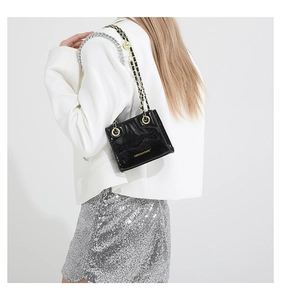 Detail of glossy black patent leather shoulder bag with golden chain strap and logo