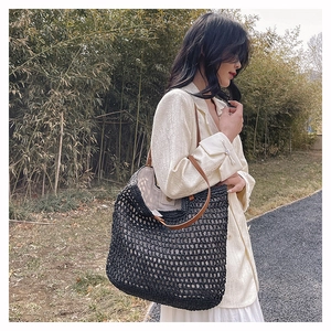 Detail of black woven tote bag with brown leather handles on a female shoulder