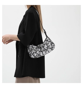 Side view of a black and white snakeskin pattern crescent shoulder bag with model