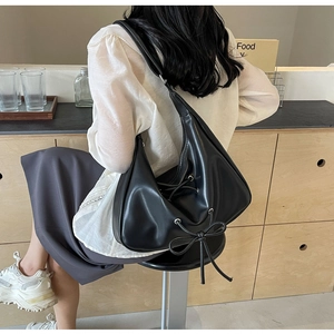 Side view of a black crescent PU leather bag with a bow detail on a fashion model