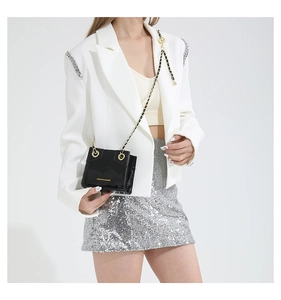 Close-up of black patent leather crossbody bag with gold chain strap on white outfit