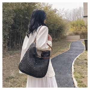Detail of a black woven hobo shoulder bag with brown leather strap in a garden setting