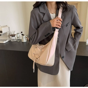 Pale pink faux leather hobo bag with drawstring bow detail worn by a model in a cafe setting