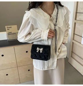 Detail of black velvet crossbody bag with silver bow accent and diamond quilting