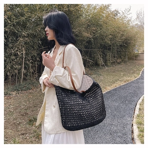 Detailed macro view of black woven tote bag with brown leather straps in outdoor setting