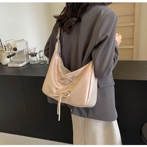Detail of cream croissant shoulder bag with lace-up bow and polished faux leather texture
