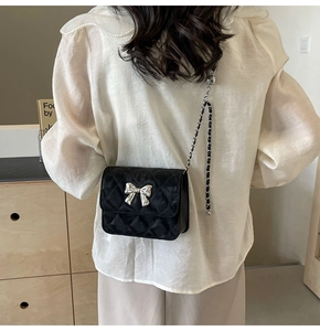 Detail of a black quilted crossbody bag with a silver bow and metal chain strap