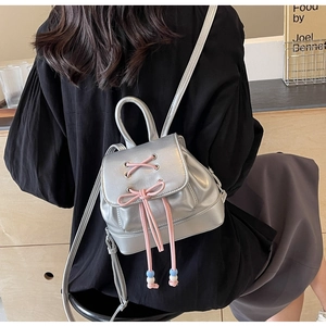 Detail of silver PU leather mini backpack featuring pink lace-up bow and bead accents