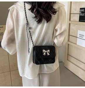 Rear view of model wearing black quilted crossbody bag with silver bow and ball charm