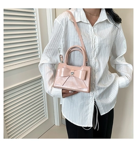 Détail du sac rose en similicuir avec nœud et boucle coeur argentée sur fond blanc